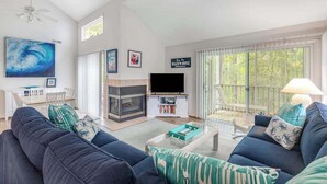 A living room with a sofa, a fireplace, a television, and a balcony. - 2-Story Sea Colony Condo w/Bikes, Fireplace, Shared Pools, Gym, Sauna, & Tennis (Bethany Beach)