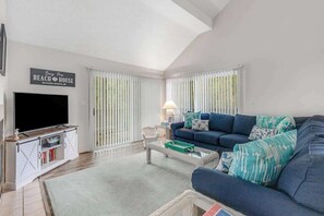 A living room with a TV, sofa, and a sign reading 'Beach House.' - 2-Story Sea Colony Condo w/Bikes, Fireplace, Shared Pools, Gym, Sauna, & Tennis (Bethany Beach)
