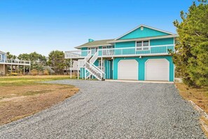A two-story house with a covered garage, a staircase leading to a balcony, and a gravel driveway. - Dog-friendly town of Fenwick home with guest suite, WiFi, & elevator (Fenwick Island)