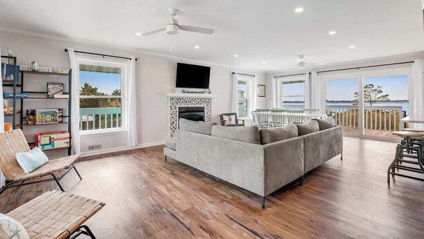 A spacious living area with a sofa, a dining table, a fireplace, and large windows offering a view of the outdoors. - Dog-friendly town of Fenwick home with guest suite, WiFi, & elevator (Fenwick Island)