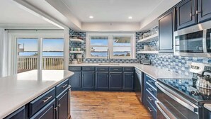 A modern kitchen with dark cabinetry, a large window with a view, and a wooden floor. - Dog-friendly town of Fenwick home with guest suite, WiFi, & elevator (Fenwick Island)