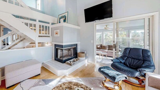 A modern living room with a fireplace, a staircase, a flat-screen TV, and a leather armchair. - Sandpiper Village home with private beach, fireplace, balcony, & washer/dryer (South Bethany)