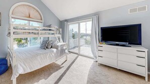 A room with bunk beds, a TV, a white dresser, and a balcony with a view. - Sandpiper Village home with private beach, fireplace, balcony, & washer/dryer (South Bethany)