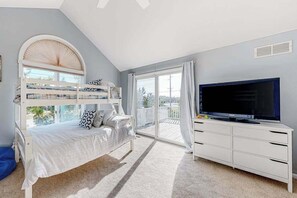 Ein Zimmer mit Etagenbetten, einem Fernseher, einer weißen Kommode und einem Balkon mit Blick.