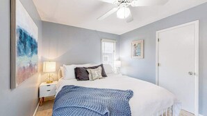 A bedroom with a bed, a nightstand, a ceiling fan, a window, and a door. - Sandpiper Village home with private beach, fireplace, balcony, & washer/dryer (South Bethany)