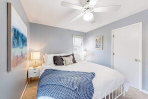 Ein Schlafzimmer mit Bett, Nachttisch, Deckenventilator, Fenster und Tür.