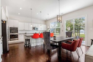 A modern kitchen with white cabinets, stainless steel appliances, and a dining area with red chairs. - Ocean View Beach Club designer home with bikes, resort-style pool, sauna & gym (Ocean View)