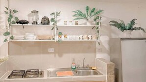 Eine Küche mit weißen Schränken, einem Edelstahlkühlschrank und Regalen mit Pflanzen und Küchenutensilien.