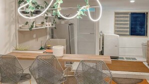 Eine moderne Küche mit Pendelleuchten, einem Essbereich mit Metallstühlen und einem sichtbaren Kühlschrank.