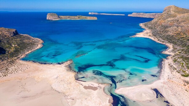 Eine Luftaufnahme einer Küstenregion mit klarem, blauem Wasser, felsigem Gelände und einem Sandstrand.