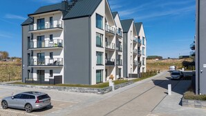A multi-story residential building with balconies, a parking area, and a clear sky. - Cozy Apartment | Air Conditioning | Balcony | Parking. (Ustronie Morskie)