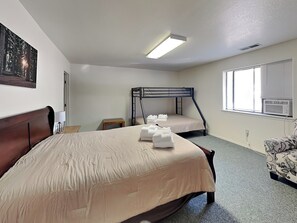 Ein Hotelzimmer mit einem großen Bett, einem kleineren Bett, einem Schreibtisch, einem Stuhl, einem Bild an der Wand und einem Fenster mit Jalousien.