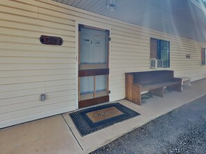 Eine Lodge mit Holztür, einer Bank davor und einer Fußmatte.