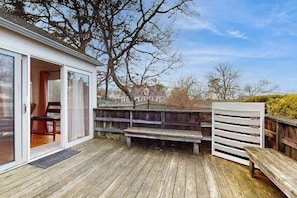 A wooden deck with a bench, a sliding glass door leading to a room, and a white fence.