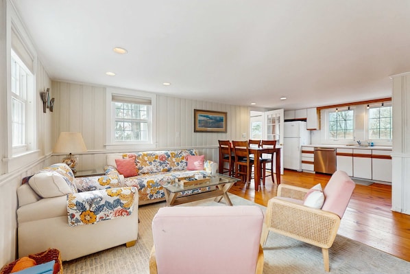 A spacious living room with a sofa, armchairs, a glass coffee table, and a dining area with chairs and a table.