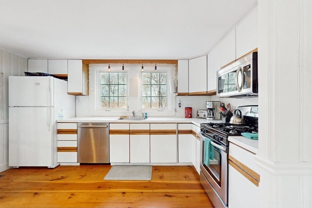 A kitchen with white cabinets, a stainless steel dishwasher, a double oven, and a window with a view of trees.