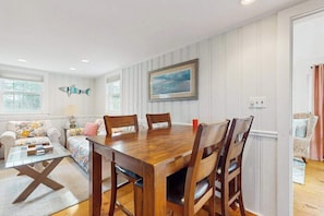 A dining area with a wooden table and chairs, a sofa with cushions, a lamp, and a framed picture on the wall.
