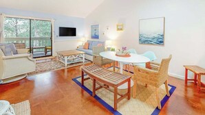 Un amplio salón con un ventanal grande, un sofá, una mesa de comedor y muebles de mimbre.