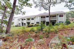 A two-story building with a front porch, a small garden with rocks and shrubs, and a tree in the foreground.