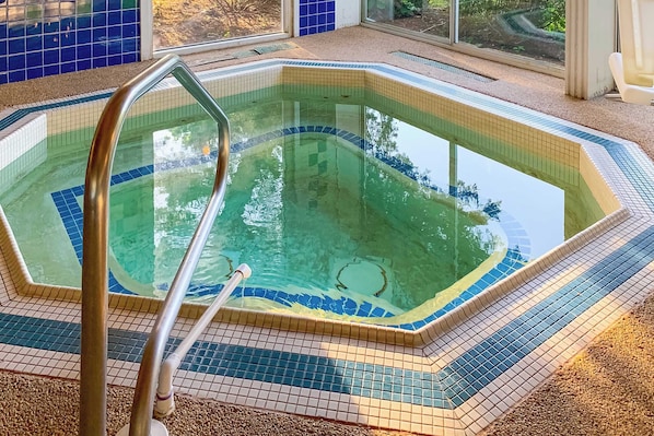 A swimming pool with a tiled edge, a metal ladder, and a view of the outdoors through large windows.