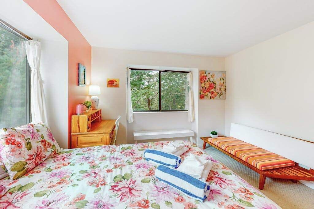 A bedroom with a bed, a bench, a desk, and a window.