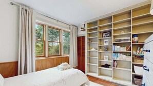 A bedroom with a bed, a large window, and a built-in bookshelf. - Dog-friendly historic home with yard, games, grill, children's items, W/D, & AC (Barnstable)