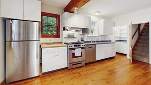 A kitchen with white cabinets, stainless steel appliances, and wooden flooring. - Dog-friendly historic home with yard, games, grill, children's items, W/D, & AC (Barnstable)