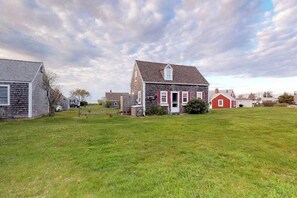 A rural setting with a single-story house, a grassy yard, and a red barn.