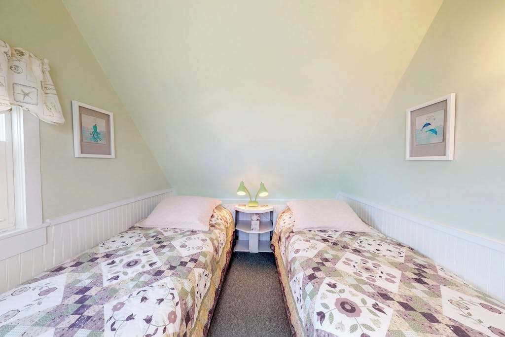 Une chambre avec deux lits simples, une petite table de chevet avec des lampes et des œuvres d’art encadrées accrochées aux murs.