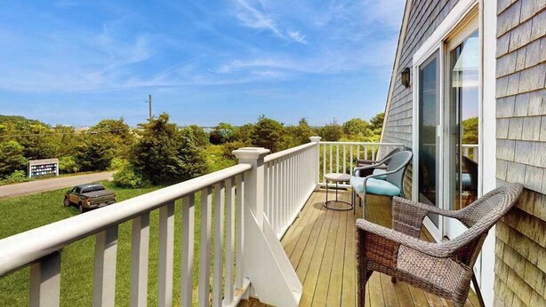 A wooden deck with a white railing, wicker furniture, and a glass door leading to a covered area. - Oceanview Buzzards Bay getaway w/ wraparound deck - steps to the Beach (Bourne)