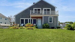 A two-story house with a balcony, a front porch, and a well-maintained lawn. - Oceanview Buzzards Bay getaway w/ wraparound deck - steps to the Beach (Bourne)