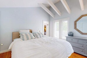 Ein Schlafzimmer mit Bett, Schminktisch, Spiegel und Fenster.