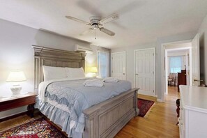 Een slaapkamer met een groot bed, een plafondventilator, een nachtkastje en een raam met gordijnen.