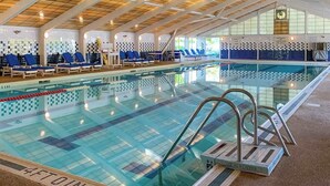 An indoor swimming pool with clear water, blue lounge chairs, and a tiled wall with a checkered pattern.