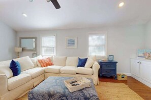 Ein Wohnzimmer mit einem Ecksofa, einem kleinen Beistelltisch, einer Lampe und einem gerahmten Bild an der Wand.