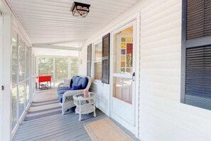 A covered porch with a wicker chair, a red table, and a window with shutters. - Welcoming home on Main St. with screened porch & large yard - 1 dog OK (Cotuit)