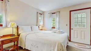 Un dormitorio con cama, mesita de noche, lámpara y puerta.