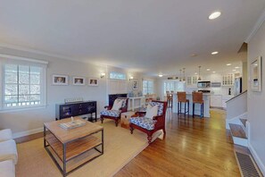 A spacious living area with a wooden floor, a dining table, two armchairs, and a sofa.