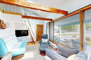 A spacious living area with a large window, a wooden ceiling, a television, and a sofa.