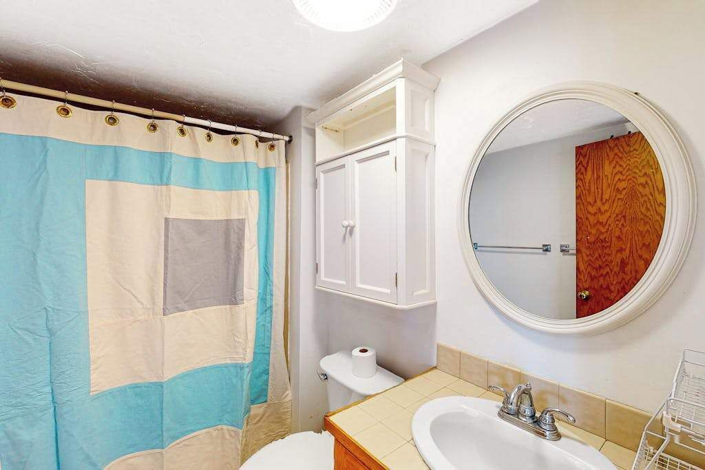 A bathroom with a shower curtain, a toilet, a sink, a mirror, and a cabinet.