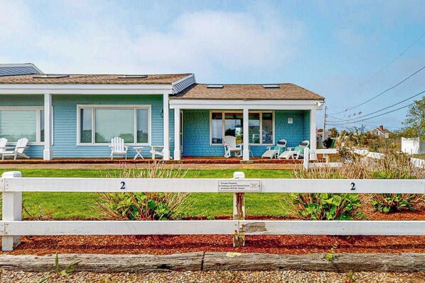 A two-story house with a porch, white chairs, and a small table.