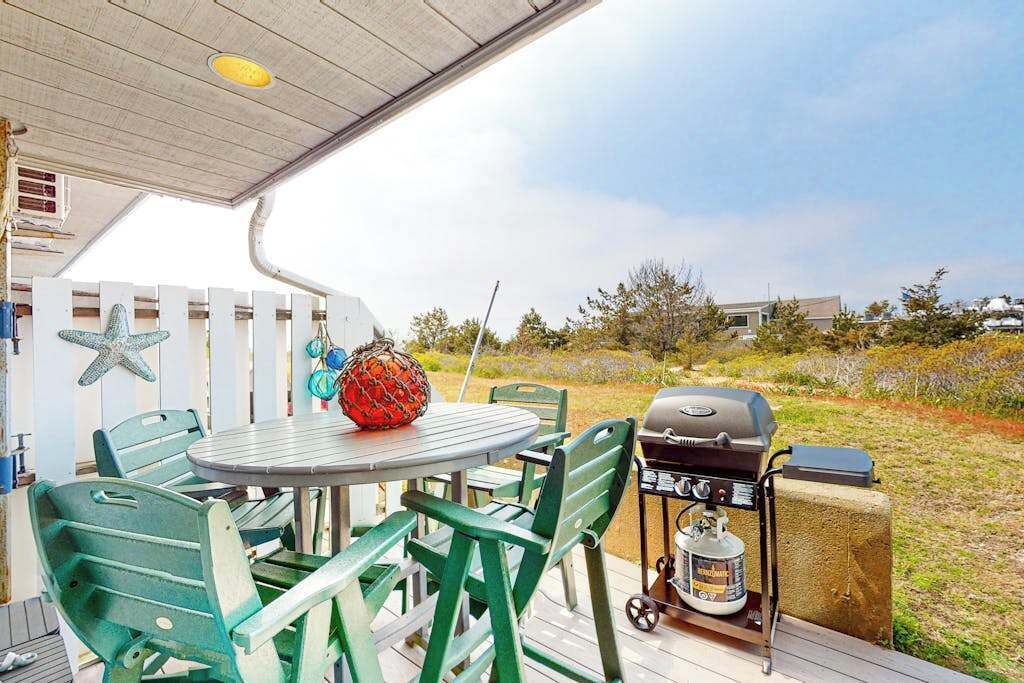 Uma área externa coberta com uma mesa redonda e cadeiras, churrasqueira e cooler.