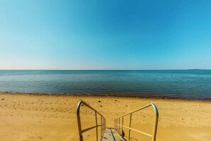 A beach with a metal staircase leading to the water, clear skies, and calm sea.