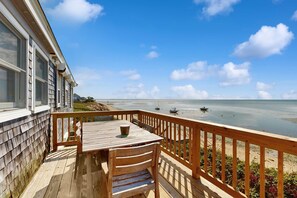 A wooden deck with a table and chairs, overlooking a beach with boats and a clear sky.