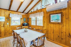 Ein Interieur einer Holzhütte mit einem Esstisch, Stühlen, einem Fernseher und gerahmten Kunstwerken.