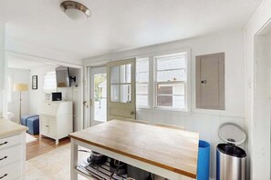Una cocina con mesa de madera, armarios blancos y un bote de basura azul.