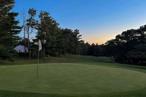Campo de golf con un mástil de bandera, rodeado de árboles y un cielo despejado.