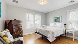 Un dormitorio con cama, cómoda, silla y ventanas.