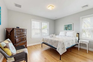 A bedroom with a bed, dresser, chair, and windows. - Newly built bayview home, steps to dock/launch on Great Pond - small dogs OK (Falmouth)