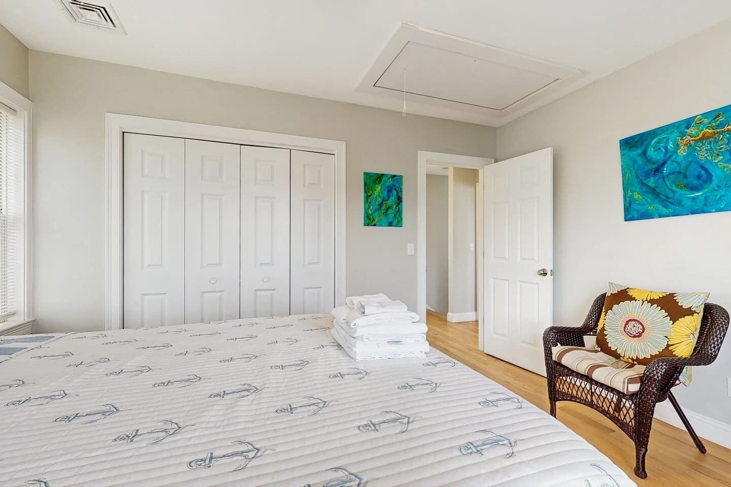 A bedroom with a large bed, white wardrobe, and a wicker chair.